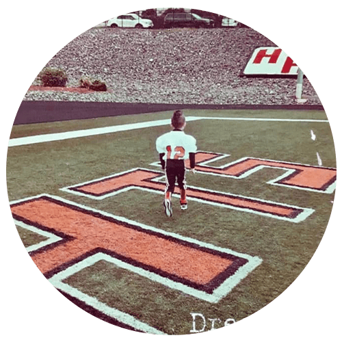 Young child in football gear running on a field towards the goal line.