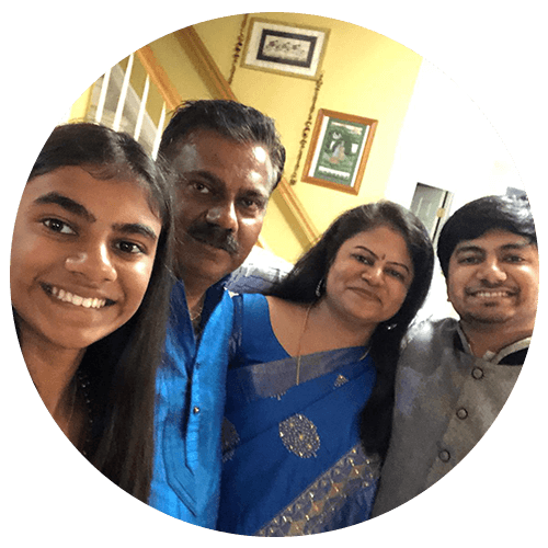 A family of four smiling, with the parents in blue traditional attire flanked by their daughter and son.